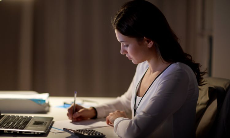 A young employee working at nigh shift  in her office is writing something in front is her laptop.