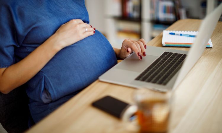 A pregnant employee is at its workplace working on her laptop.